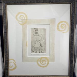 Puede incluir: Obra de arte enmarcada con una ilustración en blanco y negro de dos figuras, una con sombrero de copa. La obra está sobre un fondo blanco con espirales doradas y enmarcada en un marco oscuro y ornamentado.