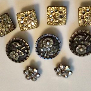 May include: Assortment of eight vintage buttons with intricate designs. The buttons are silver and gold with floral and geometric patterns.