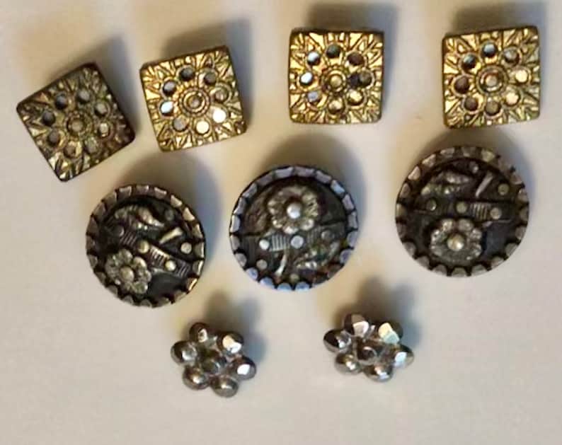 May include: Assortment of eight vintage buttons with intricate designs. The buttons are silver and gold with floral and geometric patterns.