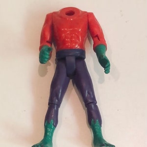 May include: A headless action figure with a red torso, purple pants, and green feet.