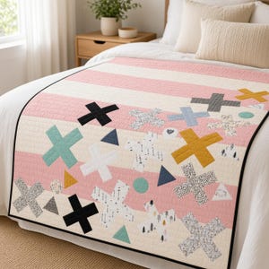 May include: A quilt featuring horizontal stripes in shades of pink and white, decorated with various appliqued shapes including crosses, triangles, and circles. The patterns on the shapes include solid colors, black and white dots, and tree motifs.