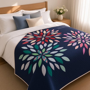 Op de afbeelding: Een marineblauwe quilt met grote, gestileerde bloemmotieven gemaakt van veelkleurige stoffen bloemblaadjes in tinten rood, roze, groenblauw, groen en lichtblauw. De quilt heeft een witte rand en ligt over een bed met witte kussens.