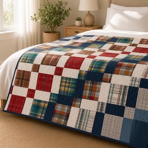 Puede incluir: Una colcha de patchwork con un patrón de cuadrícula que alterna cuadrados blancos sólidos y varios cuadrados de tela a cuadros en tonos rojos, azules, verdes y marrones. La colcha tiene un borde azul oscuro y un acolchado en forma de rombos.