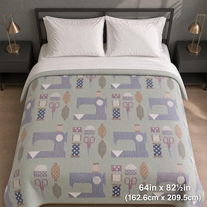 May include: A light green quilt featuring a repeating pattern of purple sewing machines, spools of thread, and scissors. The quilt measures 64 inches by 82 inches. It is draped over a bed with two white pillows and a black metal headboard.