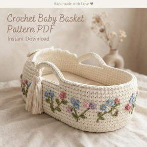 May include: An off-white crochet baby basket featuring integrated handles and a decorative tassel. The exterior is adorned with embroidered floral motifs in shades of pink, blue, and green. Text on the image reads Crochet Baby Basket Pattern PDF.