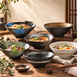 May include: A collection of ceramic bowls in various finishes, including blue, green, black, and white speckled designs. Some bowls are filled with ramen featuring soft-boiled eggs and greens, while others are empty or contain salad.