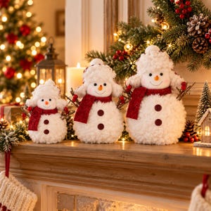 May include: Three plush snowman figurines of varying sizes, each featuring a white fuzzy texture, a red scarf, a matching hat, two dark buttons on the torso, and twig-like arms. Each snowman has a stitched face with a small orange nose.