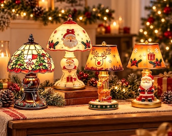 May include: Four decorative Christmas table lamps featuring festive designs. One lamp has a stained-glass style shade with trees, while the others feature Santa Claus and reindeer motifs with warm glowing light and detailed ceramic bases.