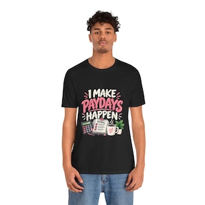 Peut inclure: Un t-shirt noir avec le texte I MAKE PAYDAYS HAPPEN en lettres roses et blanches. Le motif comprend une calculatrice, un presse-papier marqué PAYROLL avec des cases à cocher, un stylo rose, une tasse à café blanche avec un cœur et une plante verte.