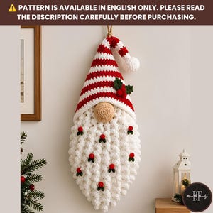 May include: A crocheted gnome wall hanging featuring a red and white striped hat with a pom-pom, a beige nose, and a long white textured beard decorated with small red berries and green leaves. Text reads: PATTERN IS AVAILABLE IN ENGLISH ONLY.