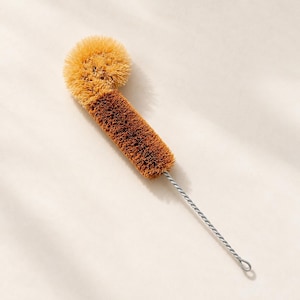 May include: A bottle brush featuring a long, twisted silver metal handle with a loop at the end. The head of the brush is composed of stiff, light brown and dark brown bristles arranged in a cylindrical shape with a rounded top.