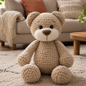 May include: A handmade crochet teddy bear crafted from light tan yarn. The plush toy features a round head with two small ears, a cream-colored muzzle, a dark brown stitched nose, and two black plastic safety eyes. The body is round and soft.