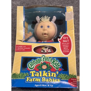 May include: A Cabbage Patch Kids Talkin' Farm Babies doll in a yellow box. The doll wears a cow-themed hood with ears and a red polka-dot outfit with a cow print. The box features text including Try Me! Press my tummy, I make REAL animal sounds!