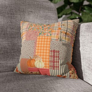May include: A square throw pillow featuring a patchwork design of various autumn-themed fabrics. The pattern includes orange gingham, floral prints, stripes, and plaid sections. Two illustrated pumpkins in orange and cream sit at the bottom.