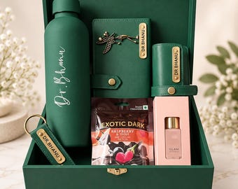 May include: A dark green gift box containing a matching matte water bottle, a notebook with a dragonfly charm, a pen case, a keychain, a small bottle of Glam perfume, and a pouch of Exotic Dark Raspberry & Goji Belgian chocolates, all personalized with the name Dr. Bhanu.