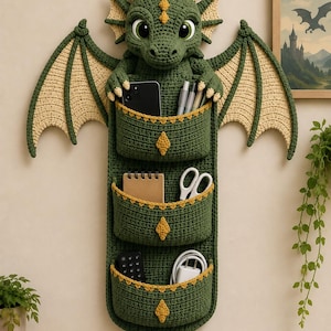 May include: A green crocheted wall organizer shaped like a dragon with large wings, horns, and a curled tail. It features three deep pockets with yellow trim, each decorated with a yellow diamond accent, designed to hold various small items.