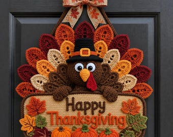 May include: A crocheted turkey wall hanging featuring a brown turkey wearing a black pilgrim hat, surrounded by a fan of colorful autumn-toned leaves. Below the turkey is a tan sign with the text Happy Thanksgiving and three orange pumpkins.
