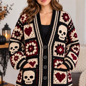 May include: A long-sleeved crochet cardigan featuring a patchwork design of black, cream, and dark red squares. The pattern includes alternating motifs of skulls, hearts, and floral shapes. The garment has a V-neckline, four black buttons, and two front pockets.