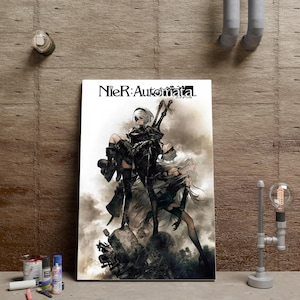 Peut inclure: Une affiche murale rectangulaire avec le logo NieR:Automata en haut. L'illustration représente deux personnages aux cheveux blancs en tenues noires, l'un portant l'autre dans un décor industriel sombre, enfumé et rempli de débris.