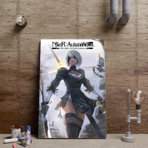 Peut inclure: Une affiche murale rectangulaire présentant le logo NieR:Automata Become As Gods Edition en haut. L'illustration représente un personnage aux cheveux blancs courts, portant un bandeau noir et une robe noire, tenant une épée près d'un petit robot.