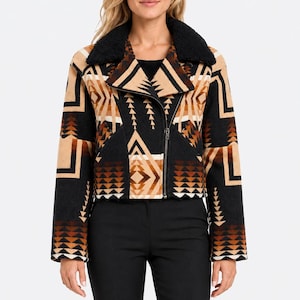 May include: A cropped jacket featuring a black, tan, and brown geometric pattern with a black sherpa collar and an asymmetrical front zipper closure. The long-sleeved garment is worn over black trousers, showcasing a structured fit and a bold, repeating angular design across the fabric.