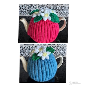May include: Two knitted teapot cosies, one pink and one blue, each decorated with white and yellow crocheted flowers and green leaves. The ribbed cosies are designed to fit snugly over a teapot, keeping the tea warm.