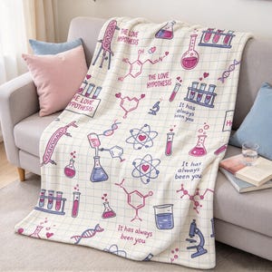 May include: A cream-colored throw blanket featuring a grid pattern and a science-themed print in pink and purple. The design includes chemical structures, beakers, test tubes, microscopes, DNA strands, and the text The Love Hypothesis and It has always been you.