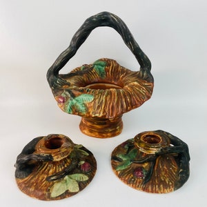 May include: A set of three ceramic candle holders and a vase, all with a rustic brown and green finish. The pieces are shaped like baskets with twisted branch handles and feature a leafy design.