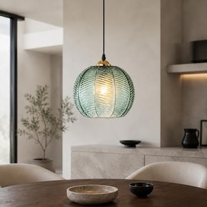May include: A spherical pendant light featuring translucent, sea-green ribbed glass with a textured, leaf-like pattern. The glass shade is suspended by a thin black cord and attached to a small, polished gold-tone metal fixture at the top.