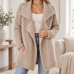 May include: A beige open-front cardigan featuring a textured waffle-knit pattern, a wide shawl collar, long sleeves, and two front patch pockets. The garment is worn over a plain white tank top and light blue denim jeans with a visible metal button.