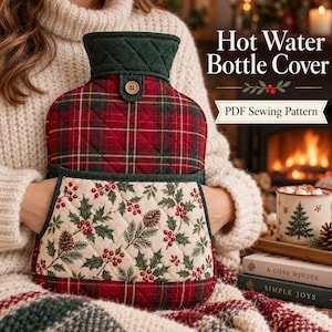 May include: A quilted hot water bottle cover featuring a red and green plaid upper section and a cream-colored lower pocket with a holly berry and pinecone print. The cover includes a dark green collar with a single wooden button.
