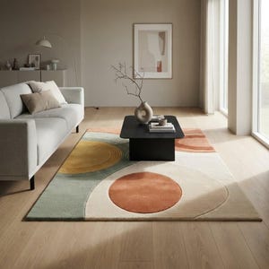 May include: A rectangular area rug featuring a geometric pattern of large circles and semi-circles in shades of mustard yellow, sage green, terracotta orange, and cream. The rug has a textured pile and is positioned on a light wood floor.