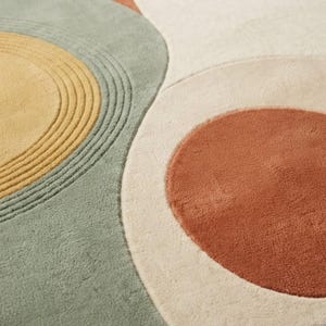 May include: A tufted area rug featuring a geometric pattern of overlapping circles and organic shapes in muted tones of sage green, mustard yellow, terracotta orange, and cream. The design includes concentric circular textures.