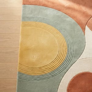 May include: A tufted area rug featuring a geometric pattern of concentric semicircles and curved shapes. The design incorporates a palette of muted terracotta, soft sage green, mustard yellow, and cream, with carved lines adding texture.