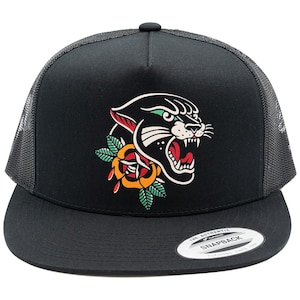 Könnte beinhalten: Eine schwarze Trucker-Cap mit Netzrückseite und flachem Schirm. Auf der Vorderseite befindet sich eine grafische Illustration eines fauchenden schwarzen Pantherkopfes über einer gelben und roten Rose mit grünen Blättern.
