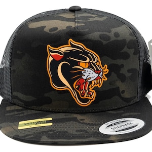 May include: A black camouflage snapback hat with a mesh back and a flat brim. The front features a graphic of a snarling black panther head with orange, red, and white details. A gold sticker on the brim reads MULTICAM BLACK and a white sticker reads SNAPBACK.