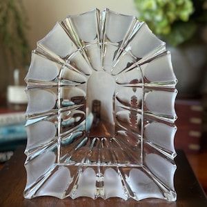 May include: A clear glass arch-shaped object featuring a series of repeating, fan-like segments with alternating smooth, transparent surfaces and frosted, matte-textured finishes, creating a radial pattern around a central open rectangular space.