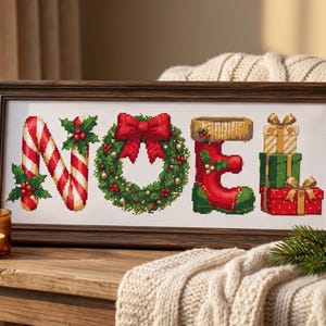 May include: A framed cross-stitch embroidery spelling the word NOEL. The letter N is a candy cane, O is a green wreath with a red bow, E is a red stocking with holly, and L is a stack of three wrapped gift boxes in gold, green, and red.