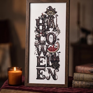 Puede incluir: Un bordado en punto de cruz enmarcado que presenta la palabra HALLOWEEN en letras grandes, oscuras y decorativas. El diseño incorpora pequeños motivos que incluyen un gato con sombrero de bruja, calaveras, una rodaja de sandía y un castillo.