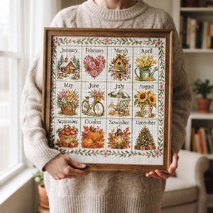 May include: A framed cross-stitch calendar featuring twelve monthly illustrations, including a snowy cabin for January, a heart of roses for February, a birdhouse for March, flowers for April, a basket for May, a bicycle for June, a beach chair for July, sunflowers for August, apples for September, pumpkins for October, a lantern for November, and a Christmas tree for December.
