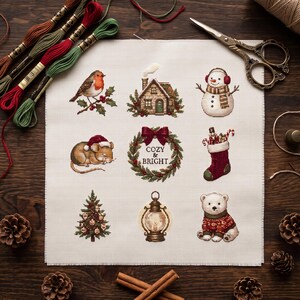 Op de afbeelding: Een vierkant stuk witte Aida-stof met een kruissteekpatroon van negen kerstmotieven: een roodborstje, een huisje, een sneeuwpop, een muis met een muts, een krans met de tekst COZY & BRIGHT, een kerstsok, een boom, een lantaarn en een ijsbeer.