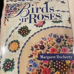 May include: A softcover book titled Birds 'n ROSES by Margaret Docherty from the Appliqué Masterpiece Series. The cover features a cream-colored quilt with intricate floral and bird appliqué designs in red, yellow, blue, and green colors.