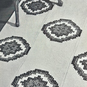 May include: A rectangular area rug featuring a light-colored, textured base with a repeating pattern of dark, geometric, star-shaped motifs. The rug is constructed with a visible braided or woven texture, and the dark motifs are arranged in a staggered layout across the surface.