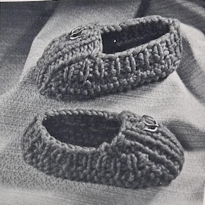 Peut inclure: Une paire de chaussons en tricot épais de couleur sombre, présentant un motif côtelé texturé sur toute la surface extérieure. Chaque chausson est orné d'une petite boucle métallique située sur la partie supérieure avant, près de l'ouverture.