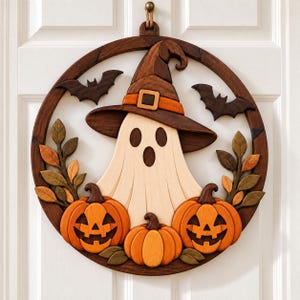 May include: A circular wooden wall hanging featuring a light-colored ghost wearing a dark brown witch hat. The design includes two dark brown bats, three orange jack-o'-lanterns, and decorative leaves arranged within a dark wood frame.