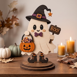 May include: A wooden ghost figurine wearing a black witch hat with a purple band and orange buckle, a purple bowtie, and black boots. The ghost holds an orange jack-o'-lantern candy bucket filled with sweets and a sign that reads "BOO!"