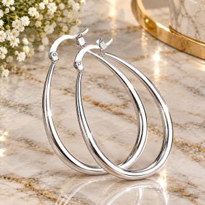 May include: A pair of polished silver-tone hoop earrings with an elongated teardrop shape. The earrings feature a smooth, reflective metallic surface and a hinged post closure mechanism at the top, designed for secure attachment to the earlobe.