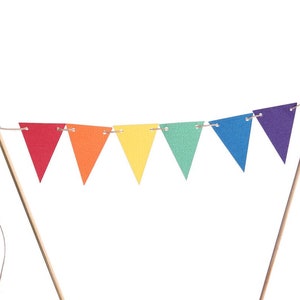 May include: A rainbow-colored paper banner with triangular flags strung on twine. The banner is attached to two wooden sticks.
