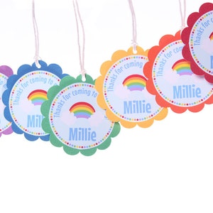 Puede incluir: Etiquetas de agradecimiento con tem&aacute;tica de arco&iacute;ris con bordes festoneados y cuerda blanca. Las etiquetas presentan un arco&iacute;ris, una nube y el texto "&iexcl;Gracias por venir a mi fiesta!" con el nombre "Millie".