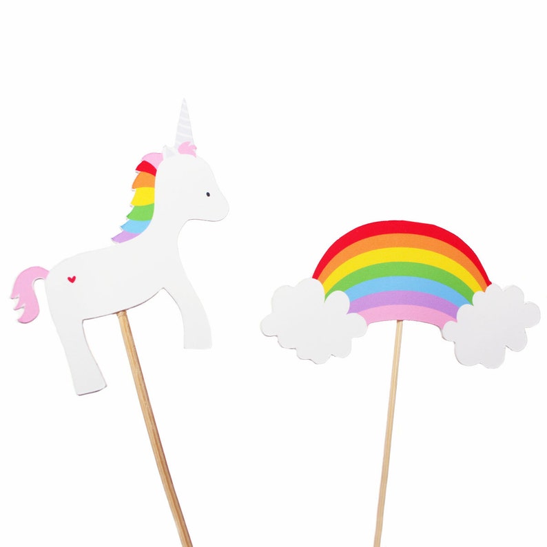 Puede incluir: Un unicornio blanco con una crin de arco&iacute;ris y un coraz&oacute;n rosa en un lado, y un arco&iacute;ris con nubes, ambos en palos de madera.